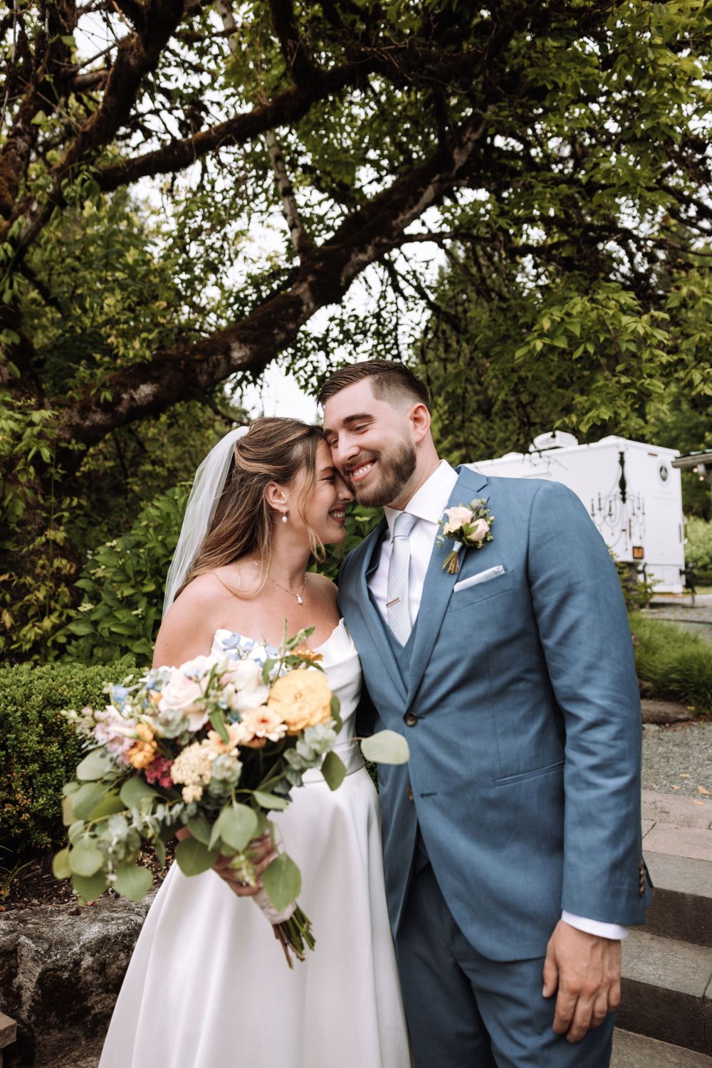 A romantic wedding portrait featuring a beautiful bouquet of peach and cream flowers in an outdoor garden setting.