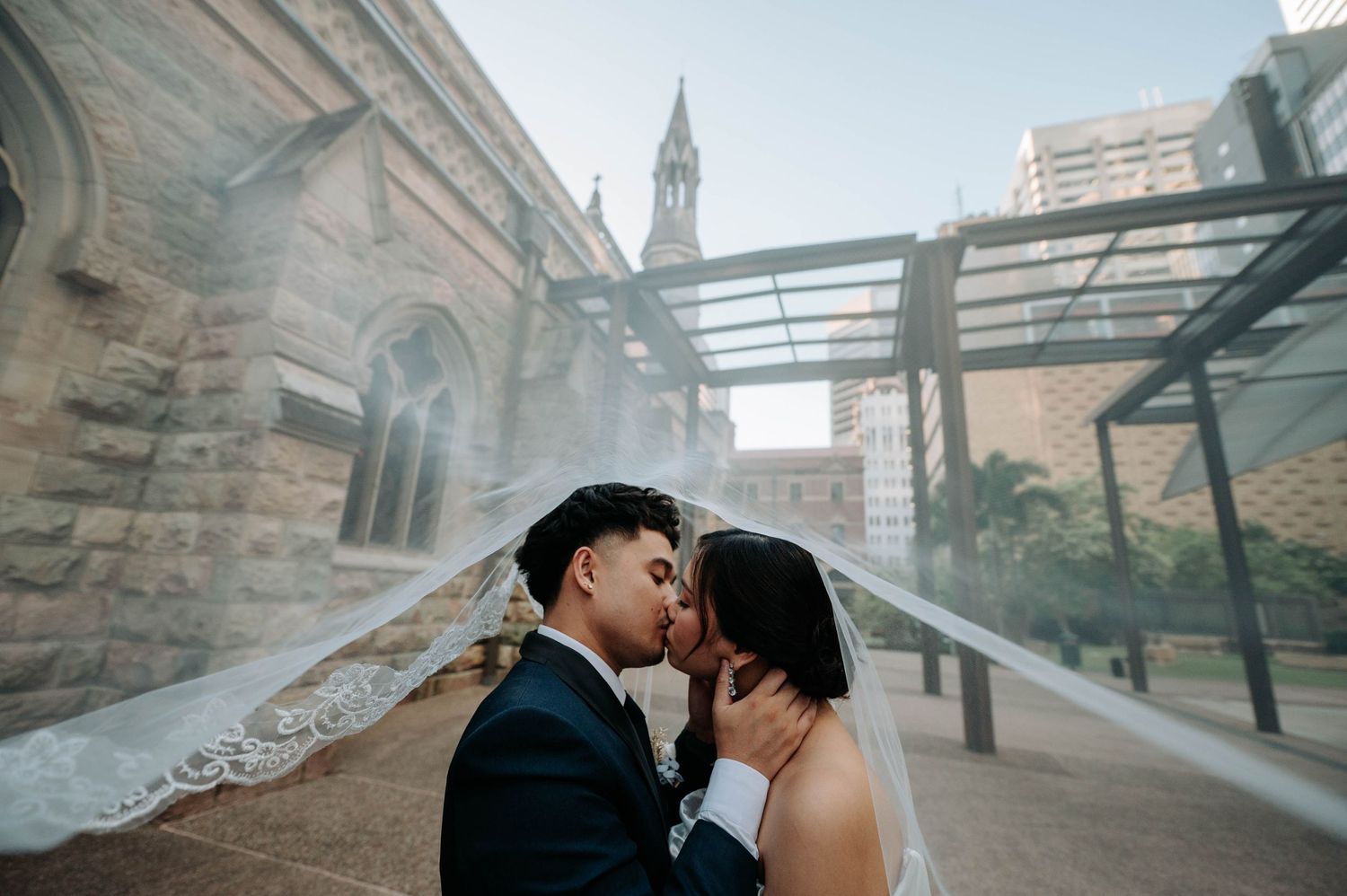 A tender moment shared between a couple under a covered walkway by a stone church.