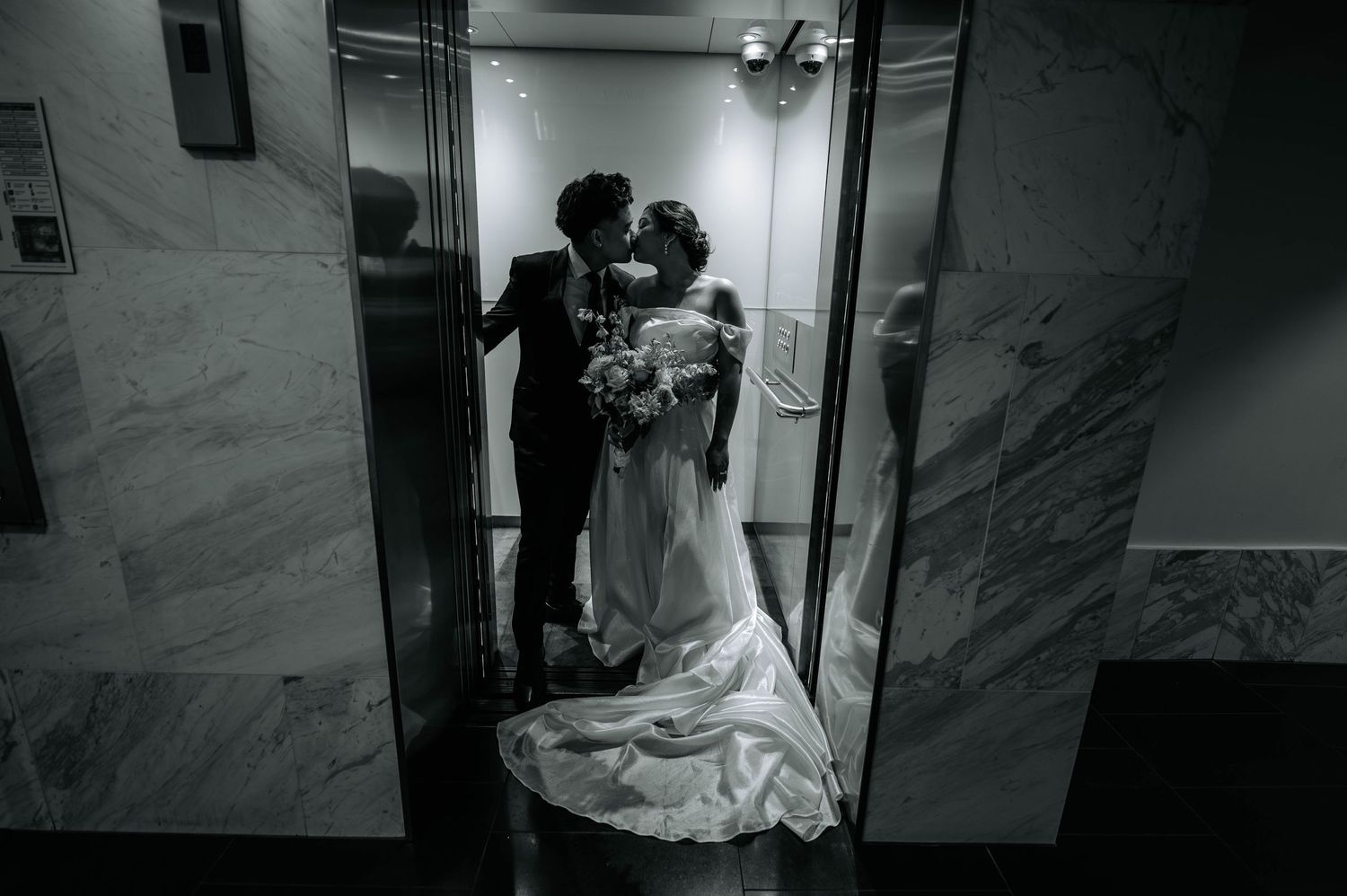 A black and white portrait of a couple sharing a moment in a marble elevator.