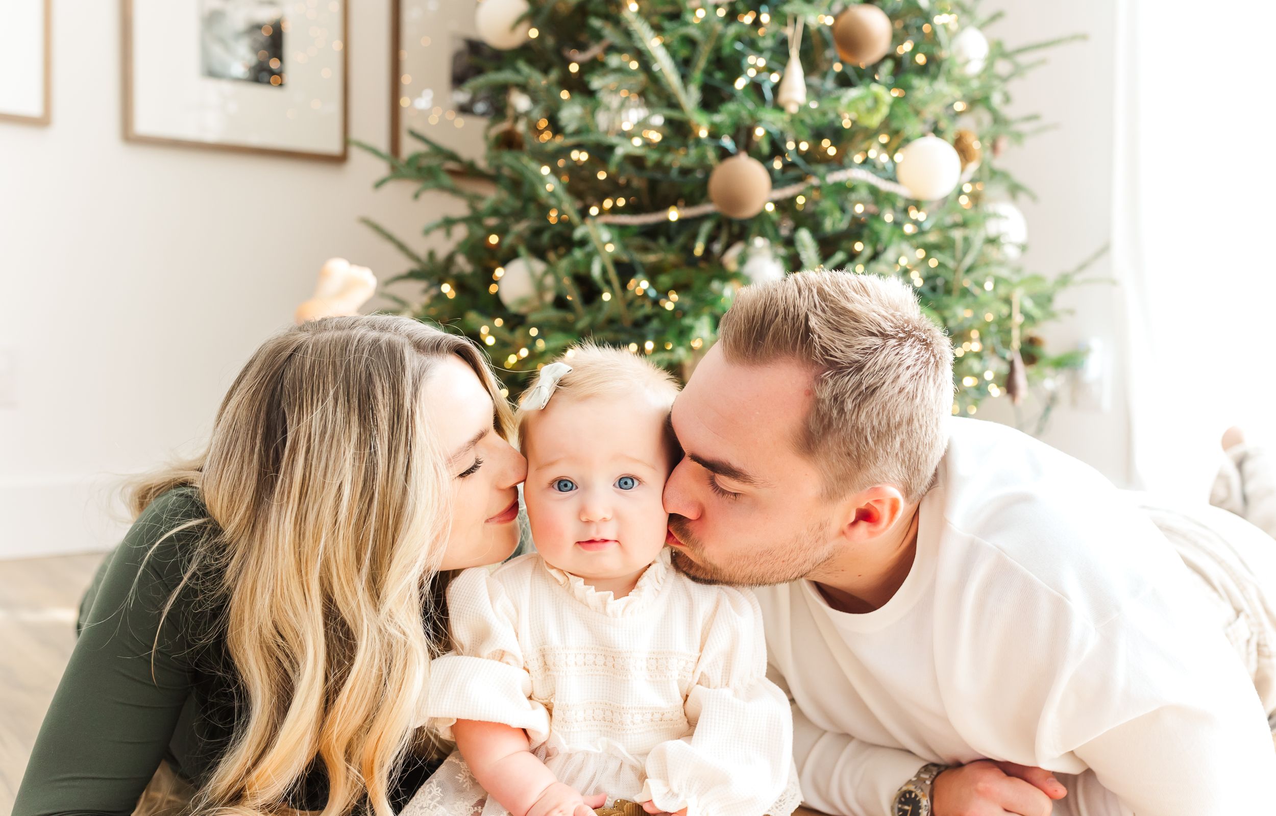 Family shares tender moment in front of decorated Christmas tree with warm lights and ornaments. PRESLEY ROSE PHOTOGRAPHY OCEAN ISLE BEACH