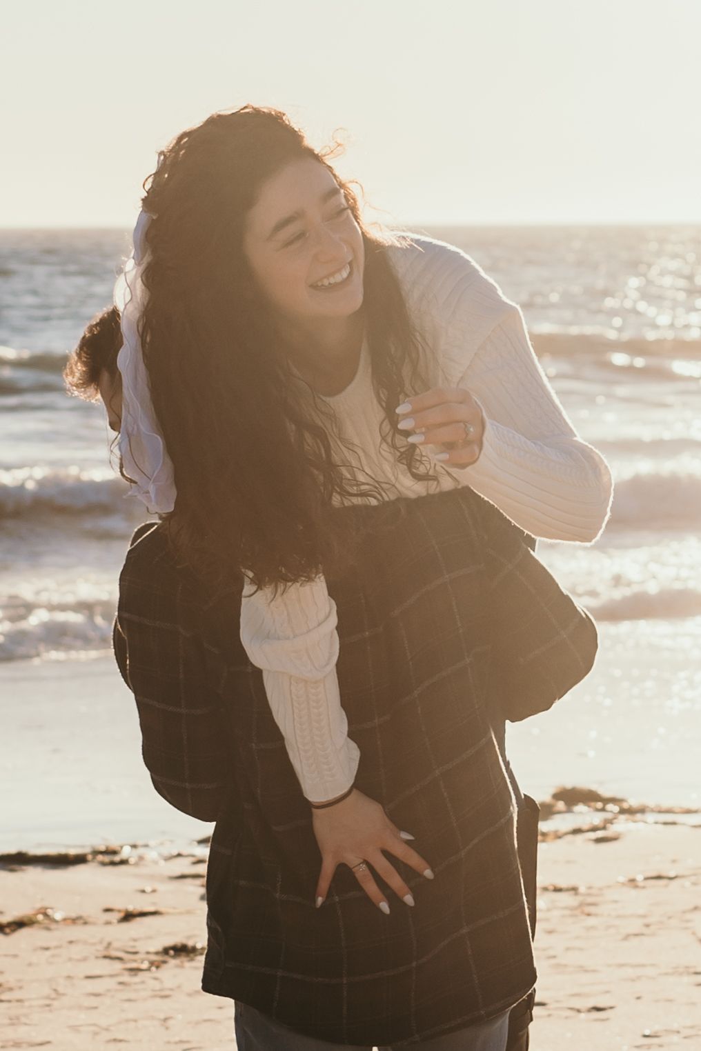 Two people share a joyful moment together on a sunny beach with ocean waves in the background.