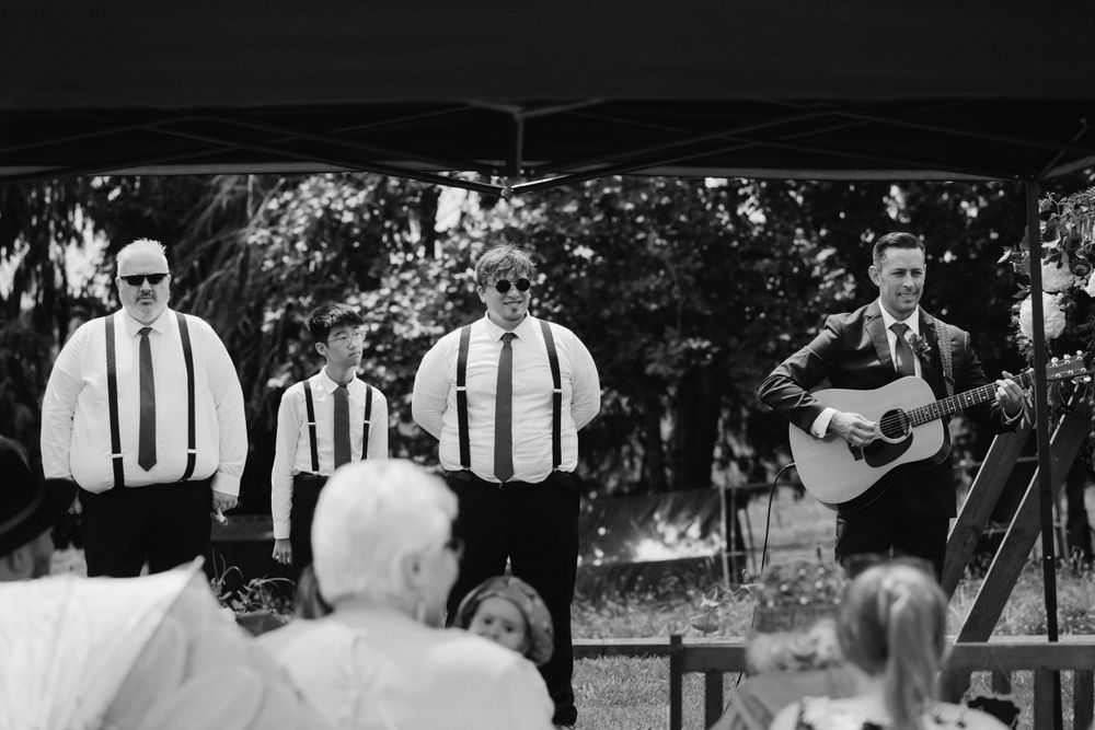 Black and white photo of a musical group performing at an outdoor event with two singers and one guitarist.
