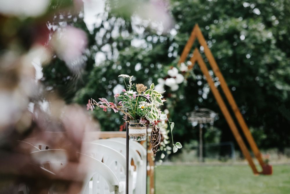 Floral arrangement decorates an outdoor wedding ceremony space with a wooden triangle arch in the background.