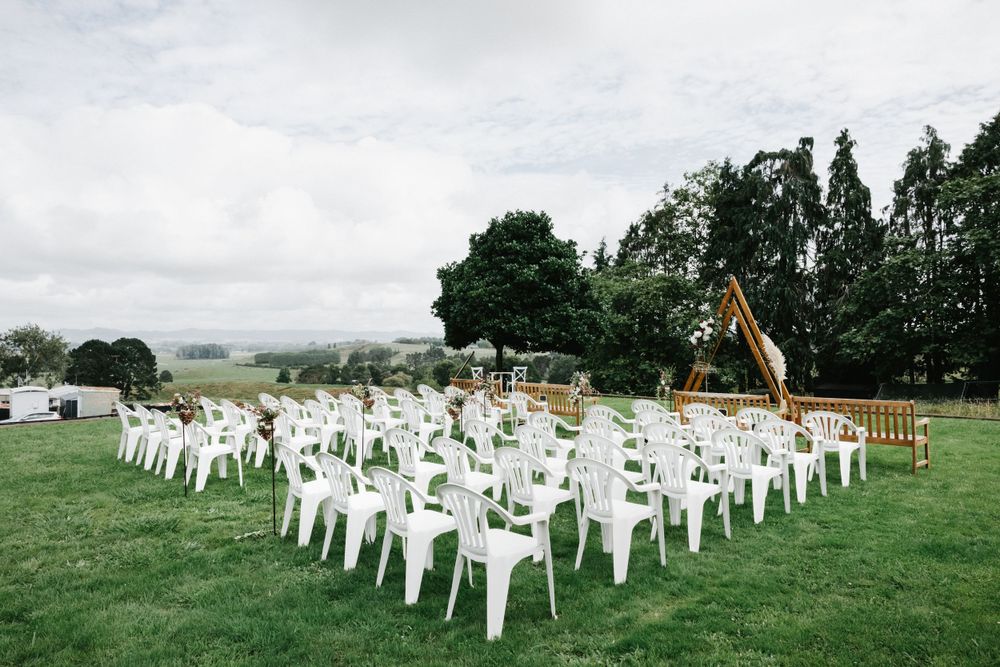 White plastic chairs arranged outdoors on a green lawn for an event setup with trees in the background.