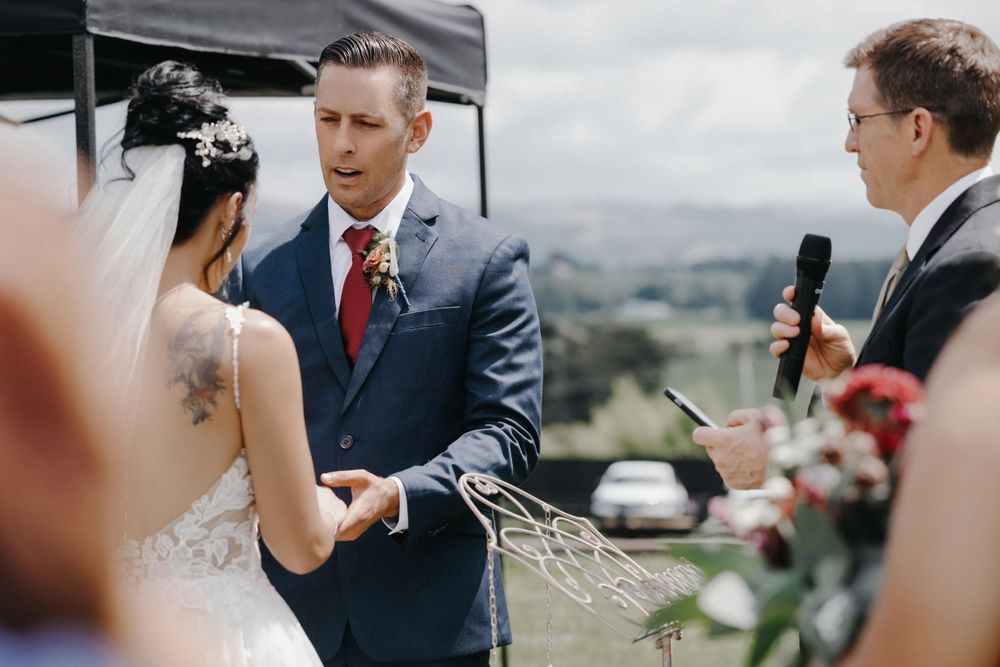 A couple exchanges wedding vows during an outdoor mountain ceremony as an officiant holds a microphone.