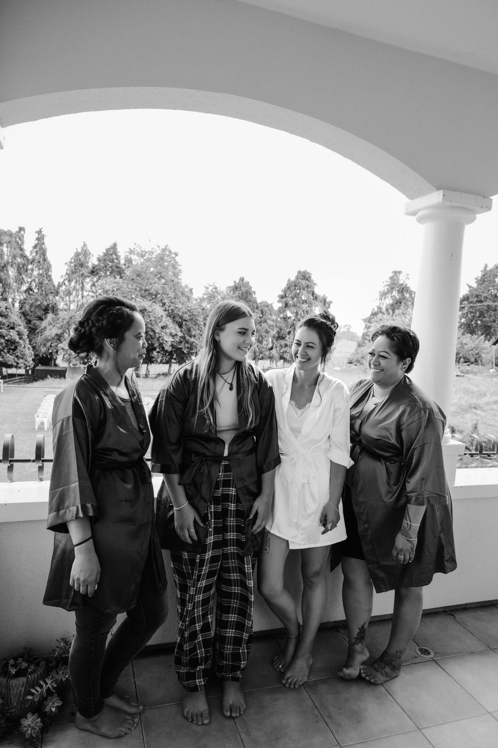 Black and white photo of four people standing together on a covered porch, dressed in casual attire.