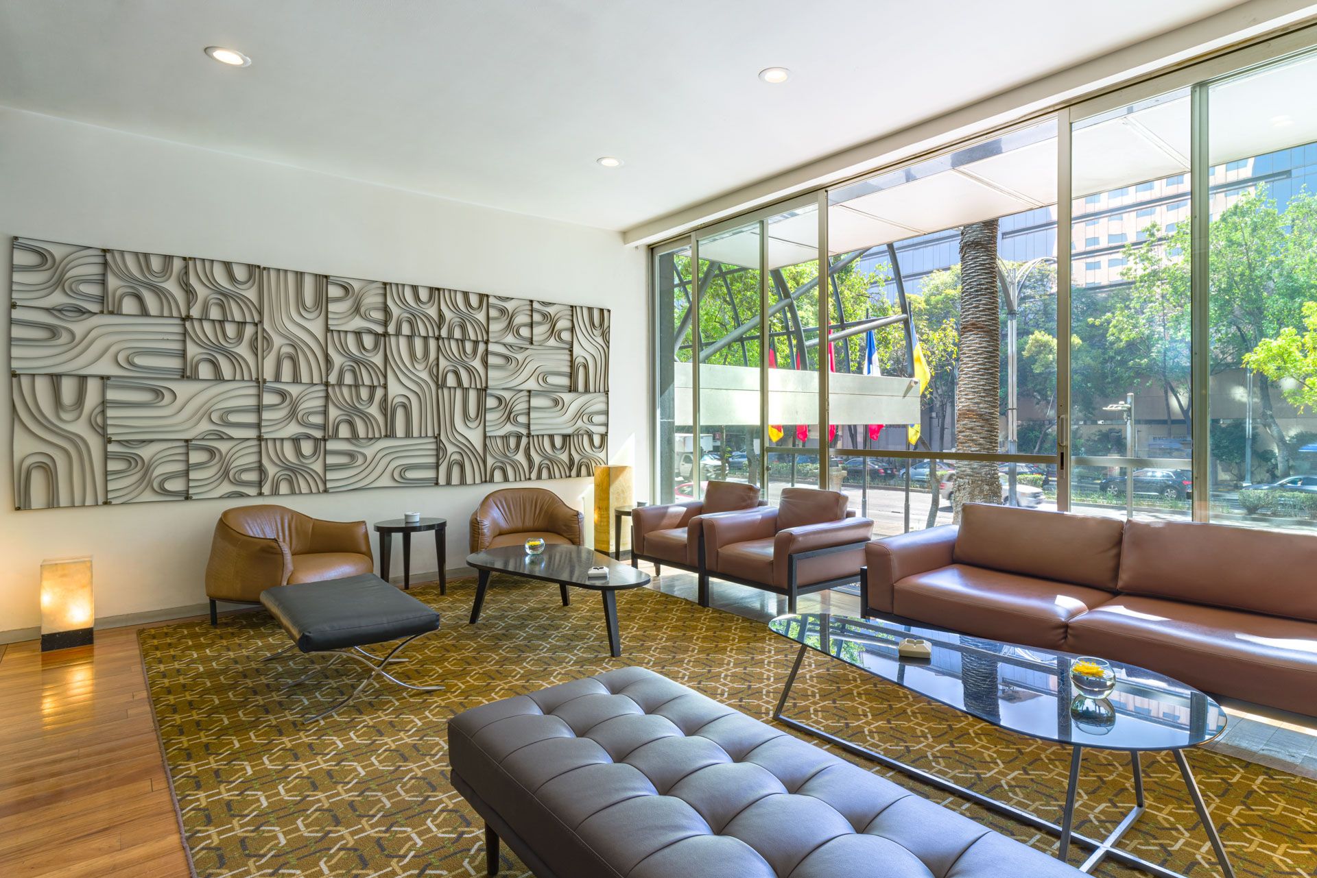 Contemporary lounge area with artistic wall design, mid-century furniture, and floor-to-ceiling windows. Barcelo Mexico Reforma.