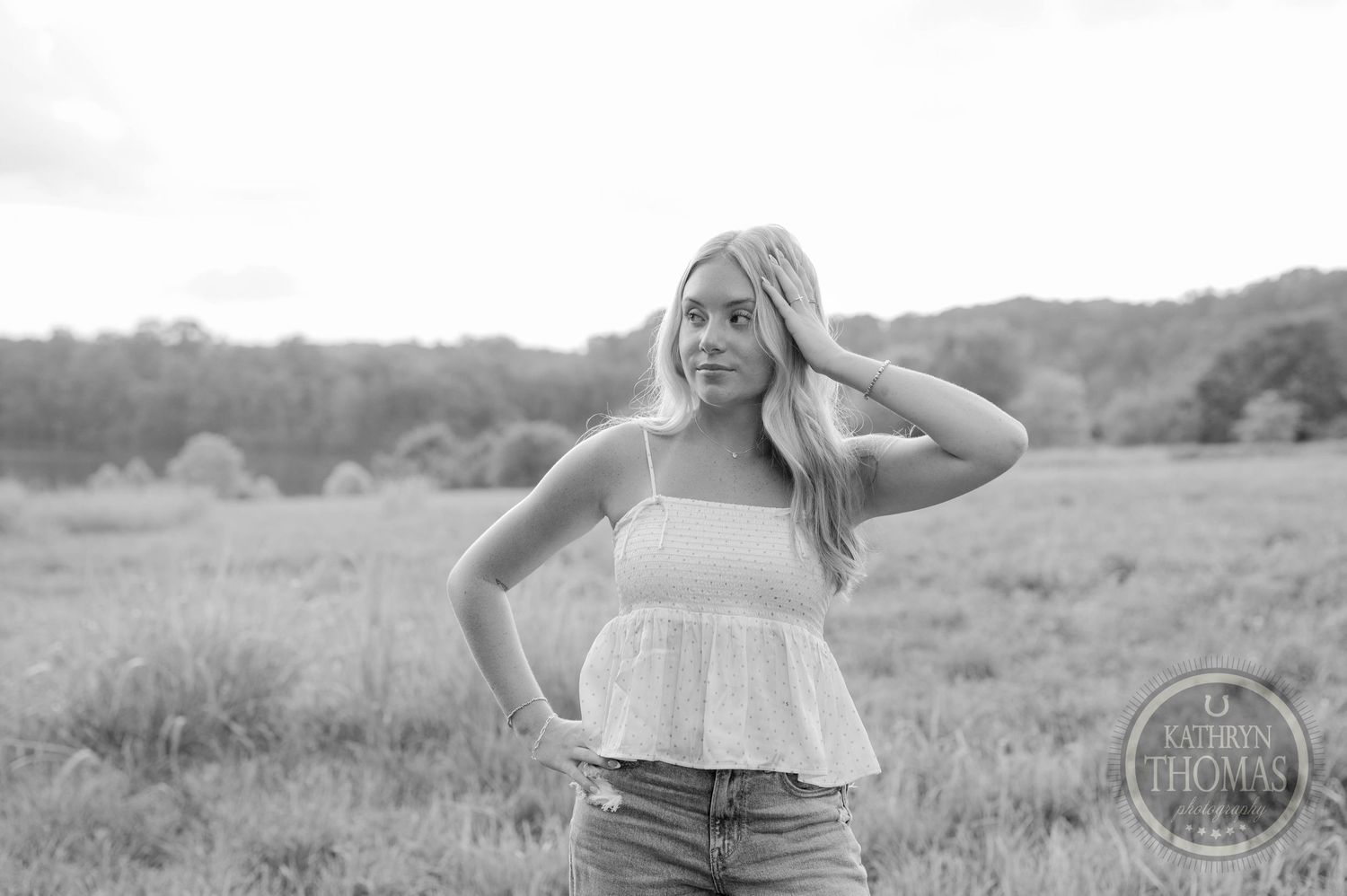 Black and white portrait in a sunny field wearing a white tank top and jeans.