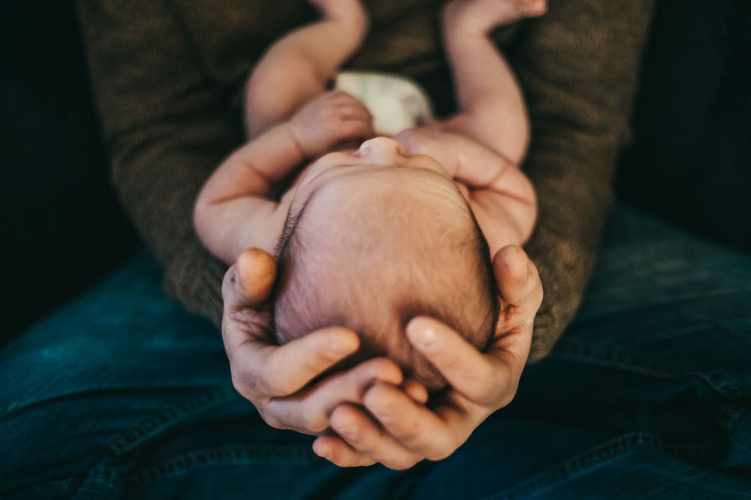 Close-up of gentle hands cradling a sleeping newborn baby.