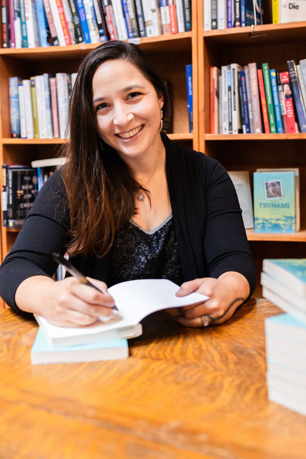 A series of photos showing someone signing books at a wooden table with bookshelves in the background.