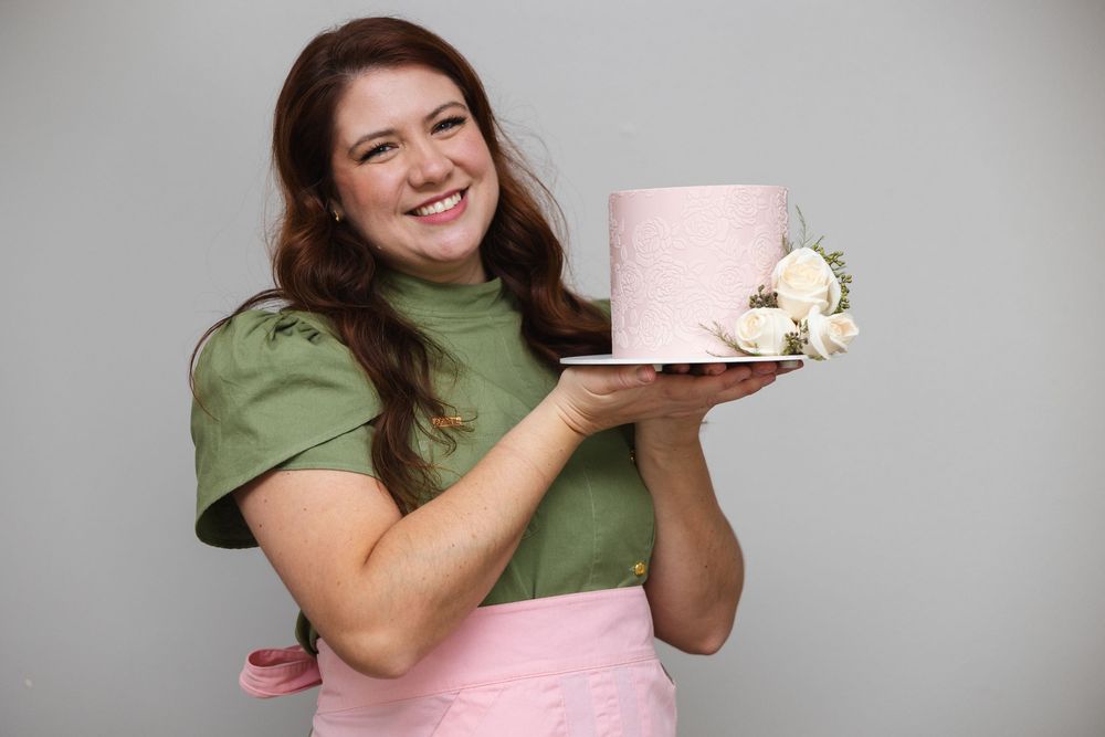 A person in a green top holds and takes bites of a large pink cotton candy treat.