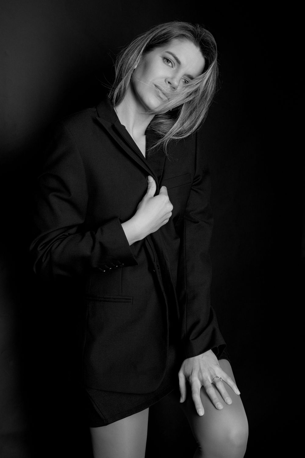 Black and white portrait of a woman in an oversized blazer posing confidently against a dark background.