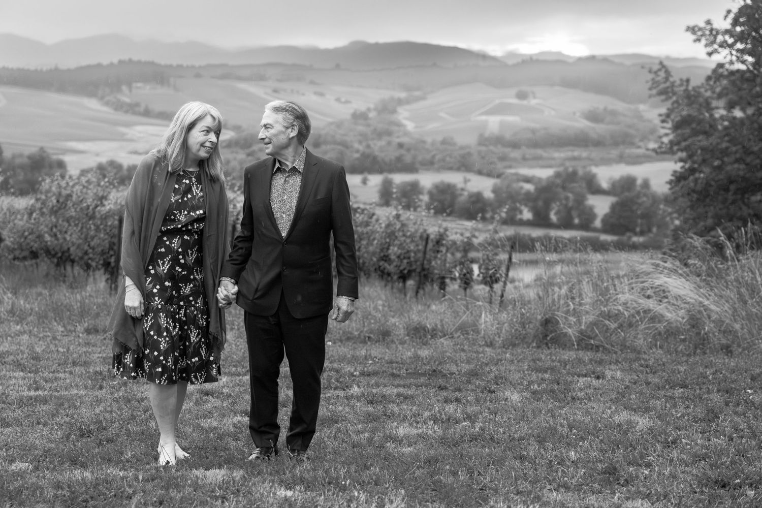 A couple walks together on a grassy hillside in a black and white romantic countryside scene.