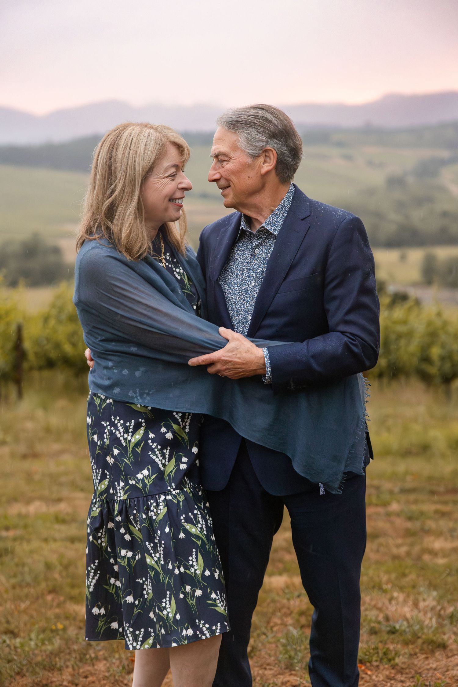 Couple shares intimate moment in field during golden hour with mountains in background.
