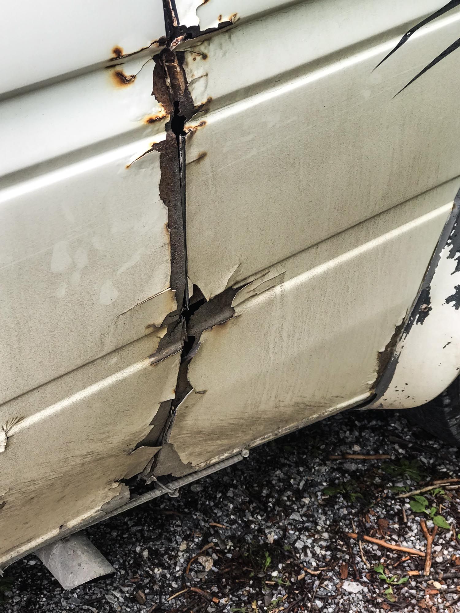 Close-up view of rotting wood siding showing progressive stages of decay and damage along a wall.