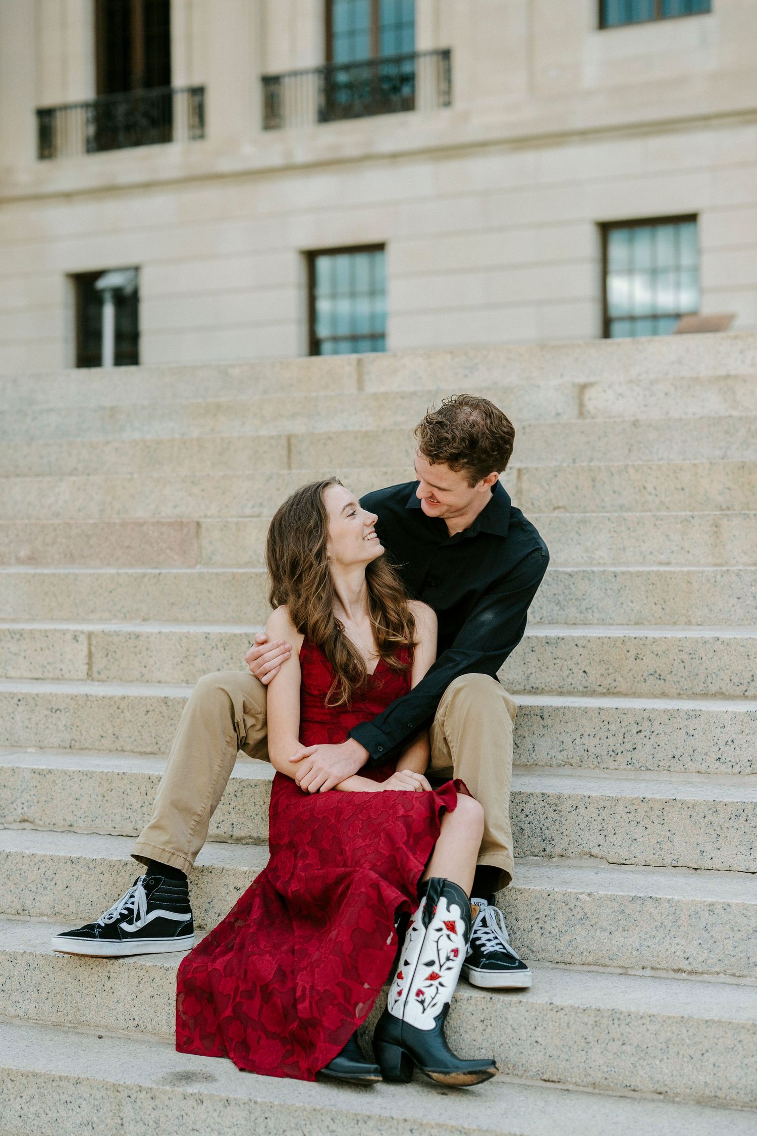 A couple in a red dress and black outfit sits romantically on concrete steps in a series of candid poses.