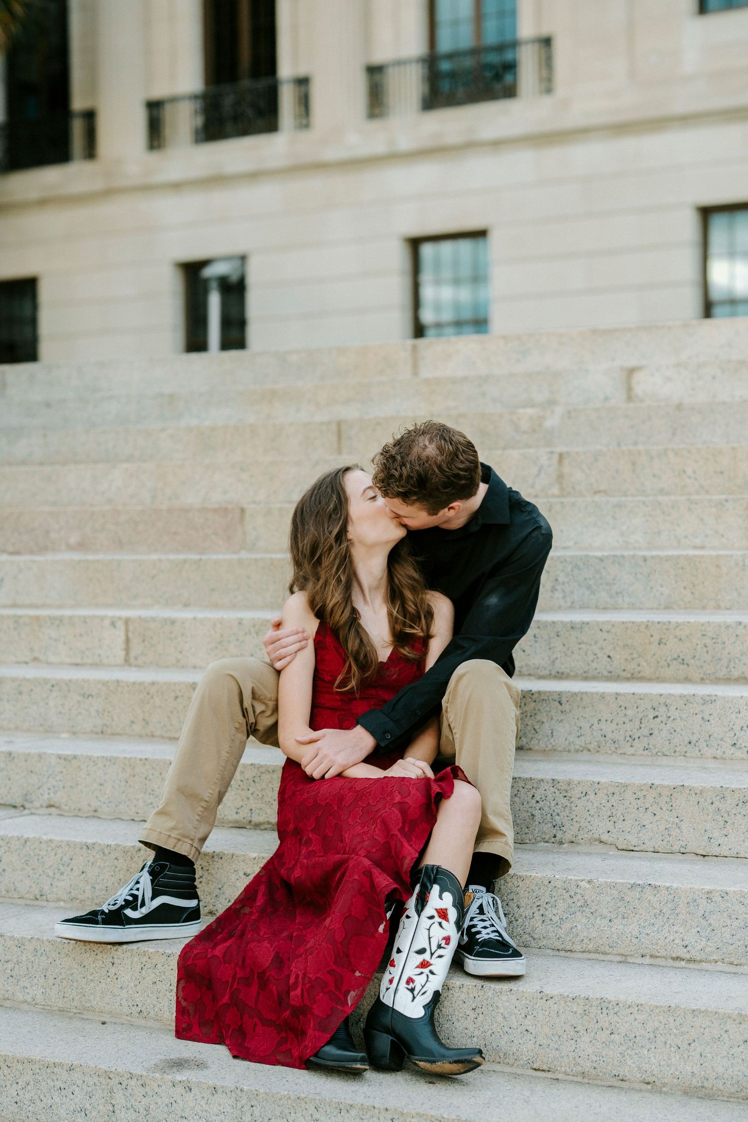 A couple shares an intimate moment while sitting on stone steps in front of a building.