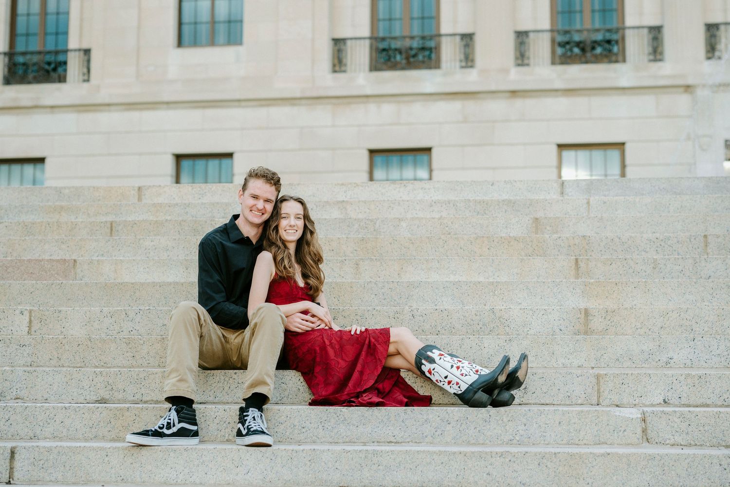 A couple sits close together on wide stone steps of a building on a sunny day.
