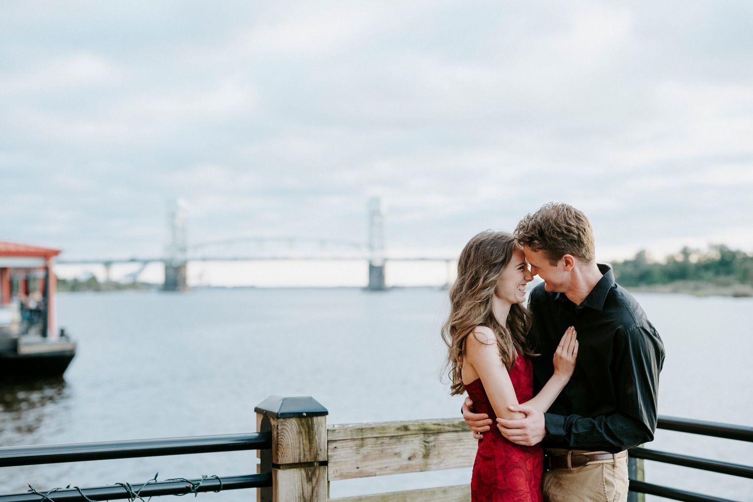 A romantic moment shared between two people on a waterfront boardwalk overlooking the ocean.