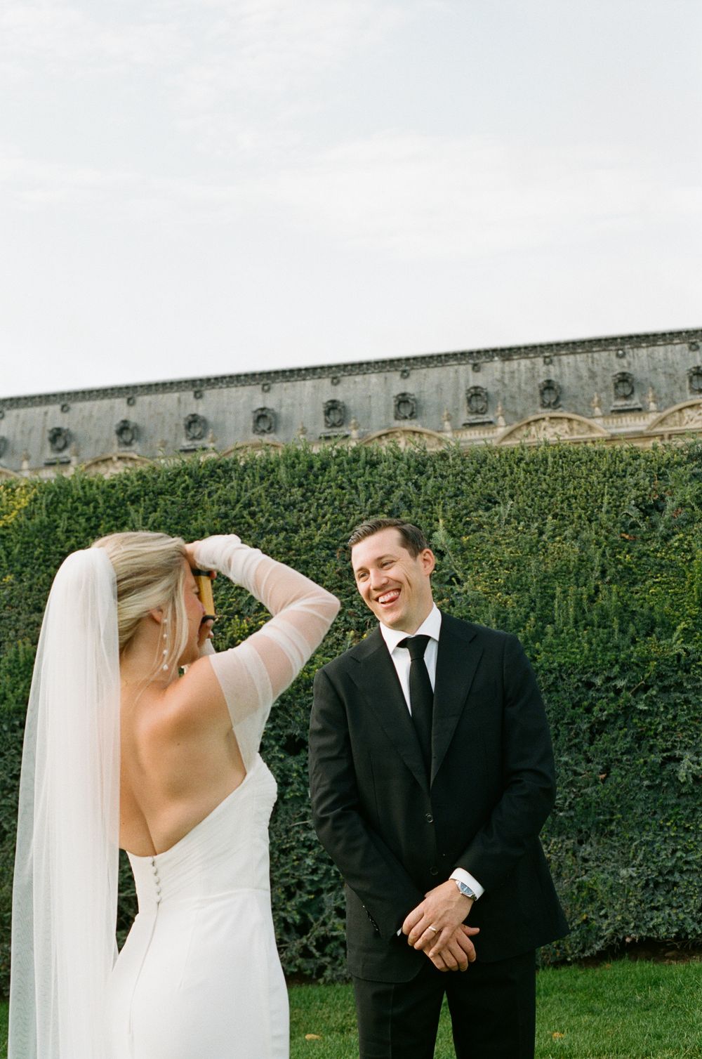 A bride and groom share a candid moment outdoors in front of an ivy-covered stone wall during their wedding. Paris editorial elopement photo