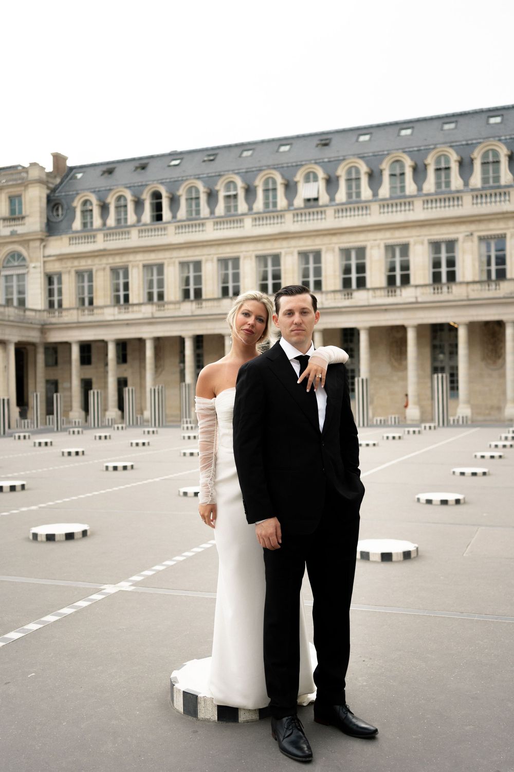 A wedding couple poses playfully in front of the Palais Royal colonnade in Paris, France. Paris editorial elopement photographer.