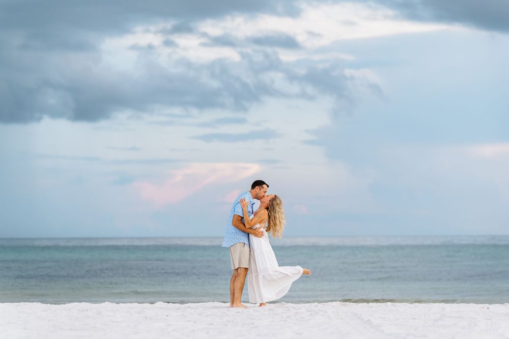 A romantic beach photoshoot at sunset with soft clouds and ocean waves in the background.
