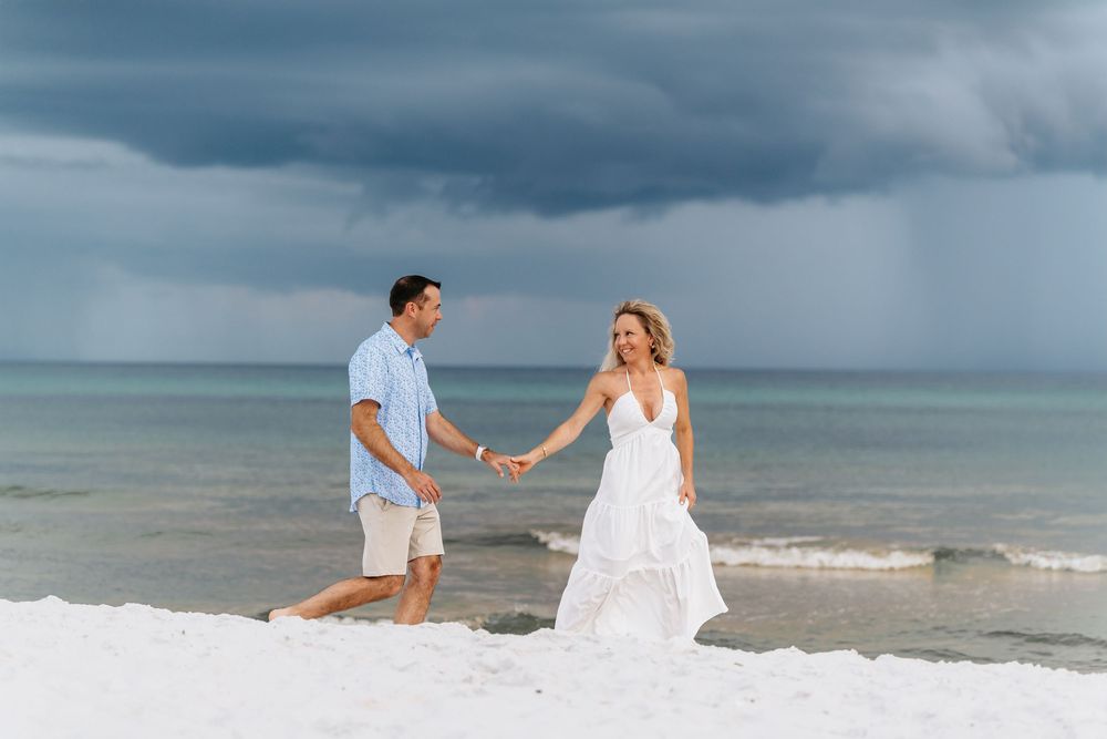Romantic beach photoshoot with stormy clouds creating dramatic backdrop over ocean waves.
