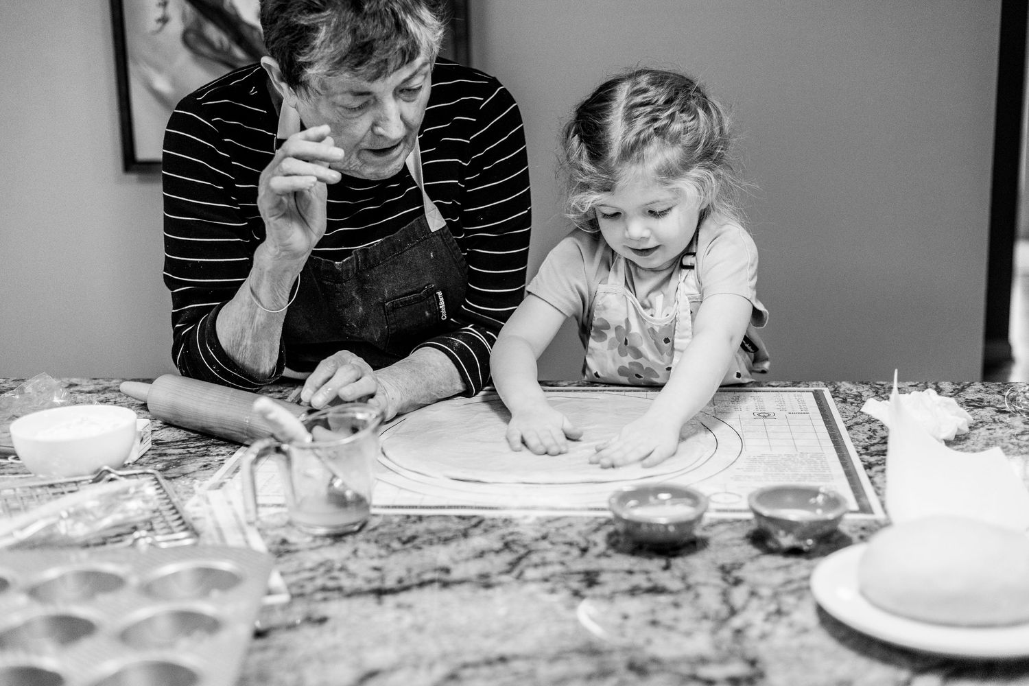 A black and white photo shows a cooking scene in a kitchen as two people work with dough on a floured surface.