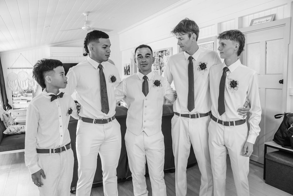 Five people in matching white formal attire share a candid moment together indoors.