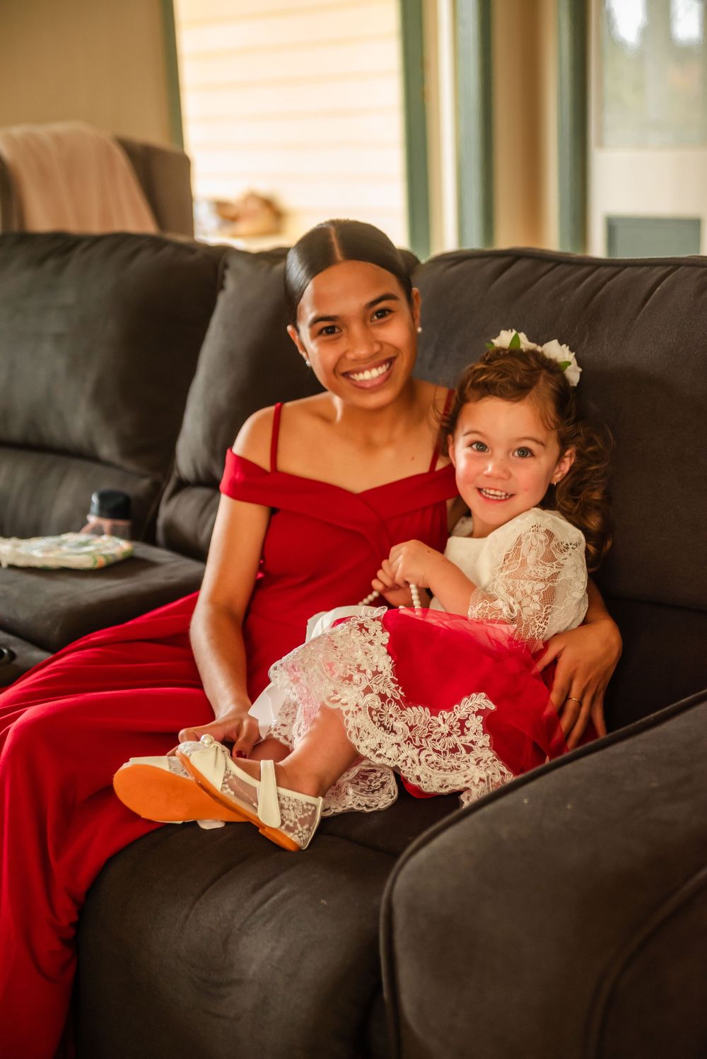 A touching moment between two people wearing red and white lace dresses seated on a dark couch.