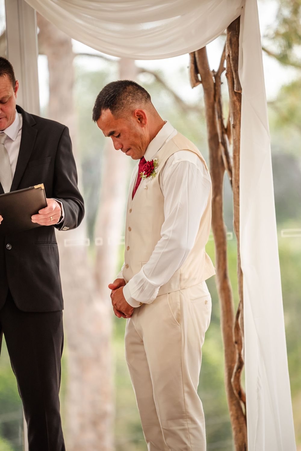 Wedding party members in white and black suits adjusting their attire under draped white fabric.