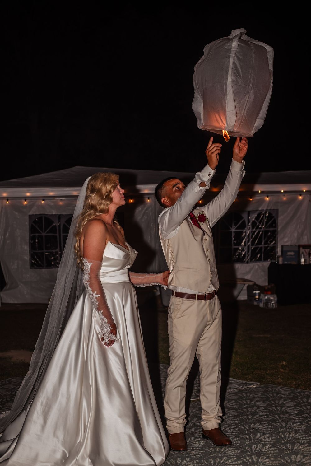 A couple dances joyfully at their wedding reception in the evening, with the bride wearing a flowing white gown.