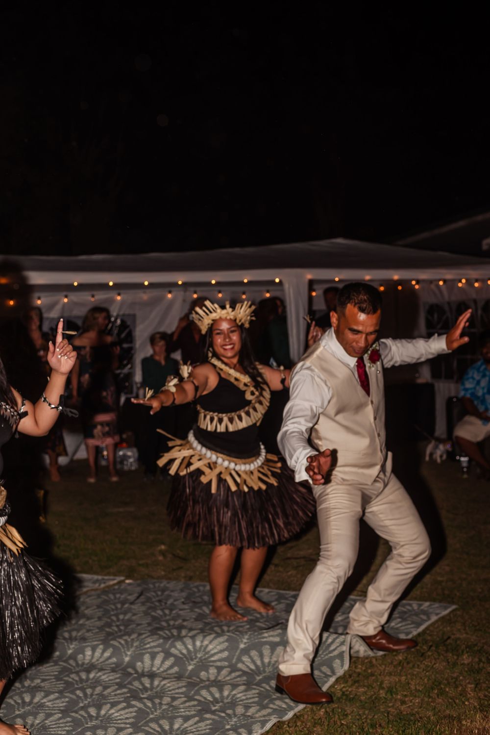Wedding guests dance energetically on a dance floor under string lights at an outdoor evening reception.
