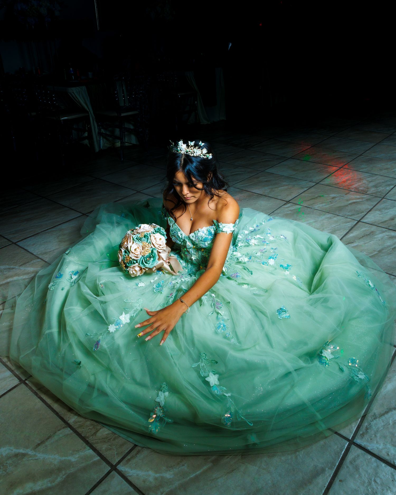 Mint green formal gown with delicate embellishments photographed on dark tile floor.