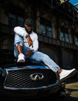 Confident man in white shirt and jeans poses on Infiniti luxury car hood.