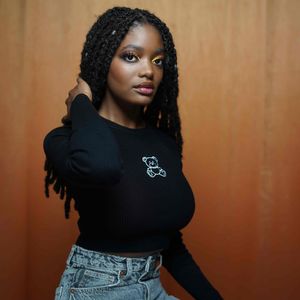 Young Black woman in black crop top with bear embroidery poses against orange background.