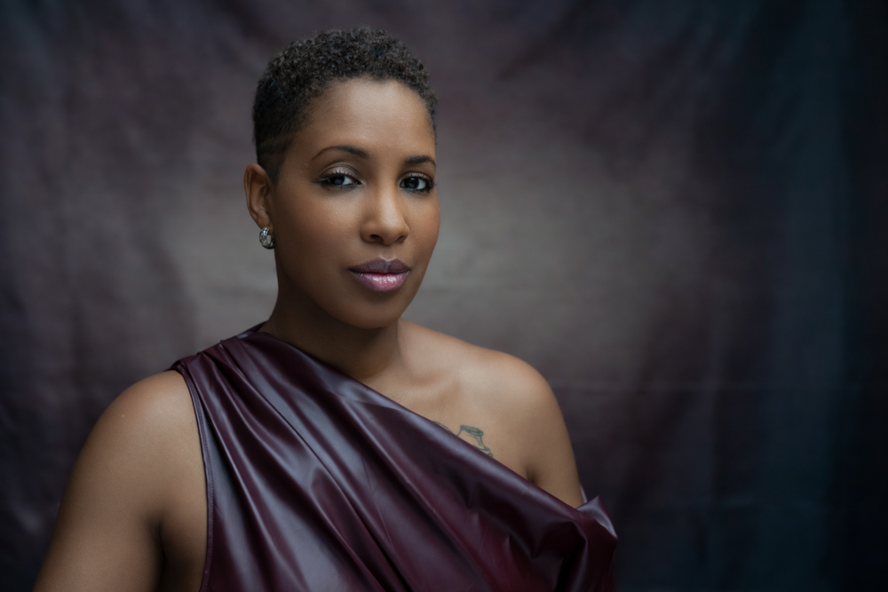 A beautiful woman in a elegant burgundy draped dress poses for a professional portrait photo.