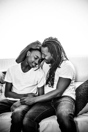 Black and white photo of affectionate couple sitting close together on couch sharing intimate moment.