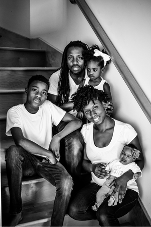 Black and white family portrait of five on staircase, parents with three children including newborn.