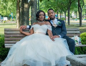 Happy wedding couple in formal attire sit together on park bench outdoors.