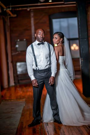 Elegant bride and groom in formal wedding attire pose in rustic loft venue.