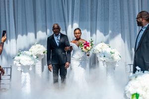 Bride in fitted white gown being escorted down the aisle through dramatic fog at an elegant wedding ceremony.