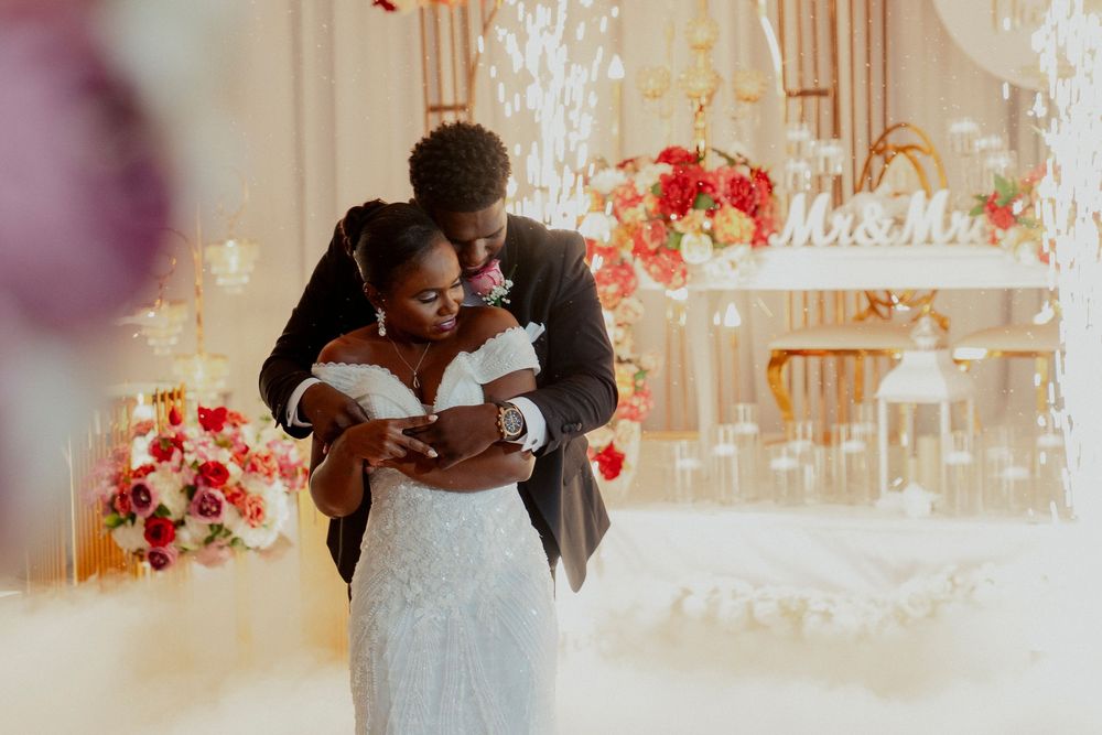Groom tenderly embracing bride in beaded gown during first dance at a lavishly decorated wedding reception.