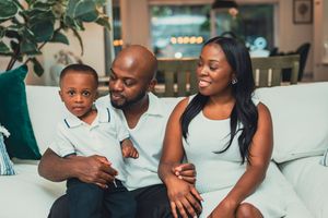 Happy Black family with young son sitting together on white sofa in bright modern living room.