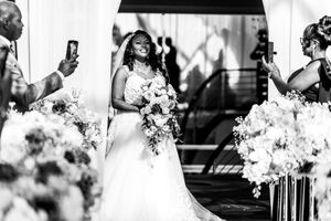 Radiant Black bride walks down aisle holding bouquet at elegant outdoor wedding ceremony.