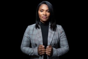 Professional Black woman in plaid blazer poses confidently against dark background.