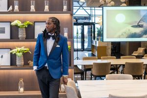 Stylish man in blue tuxedo with bow tie stands in modern hotel lobby.