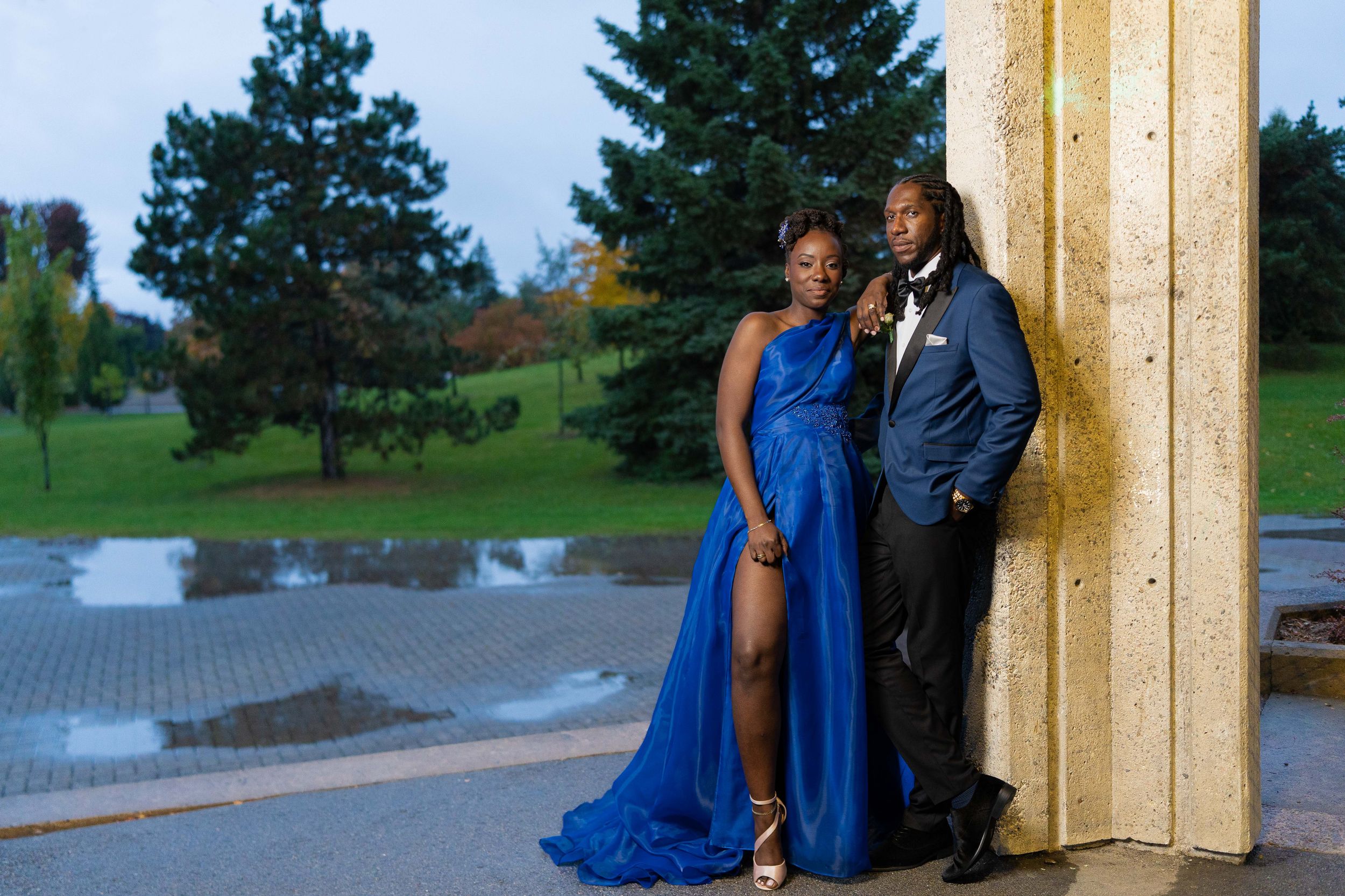 Elegant couple in matching royal blue formal attire pose outdoors at dusk.