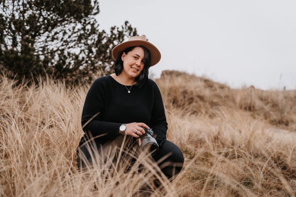 Person in black attire and brown hat sitting in tall grass on a hillside.