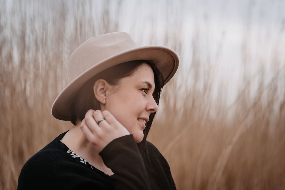 Side profile portrait in brown hat against blurred natural backdrop.